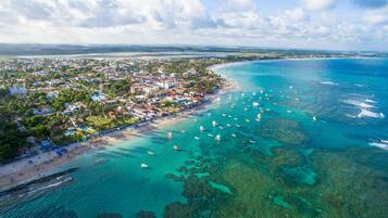 An aerial view of a coastal town with a beach, clear waters, and numerous boats.