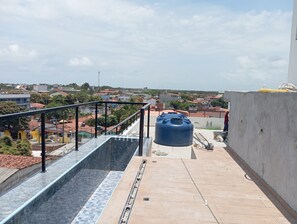 A rooftop terrace with a metal railing, a blue water tank, and a view of a residential area. - Varandas do Porto (Ipojuca)