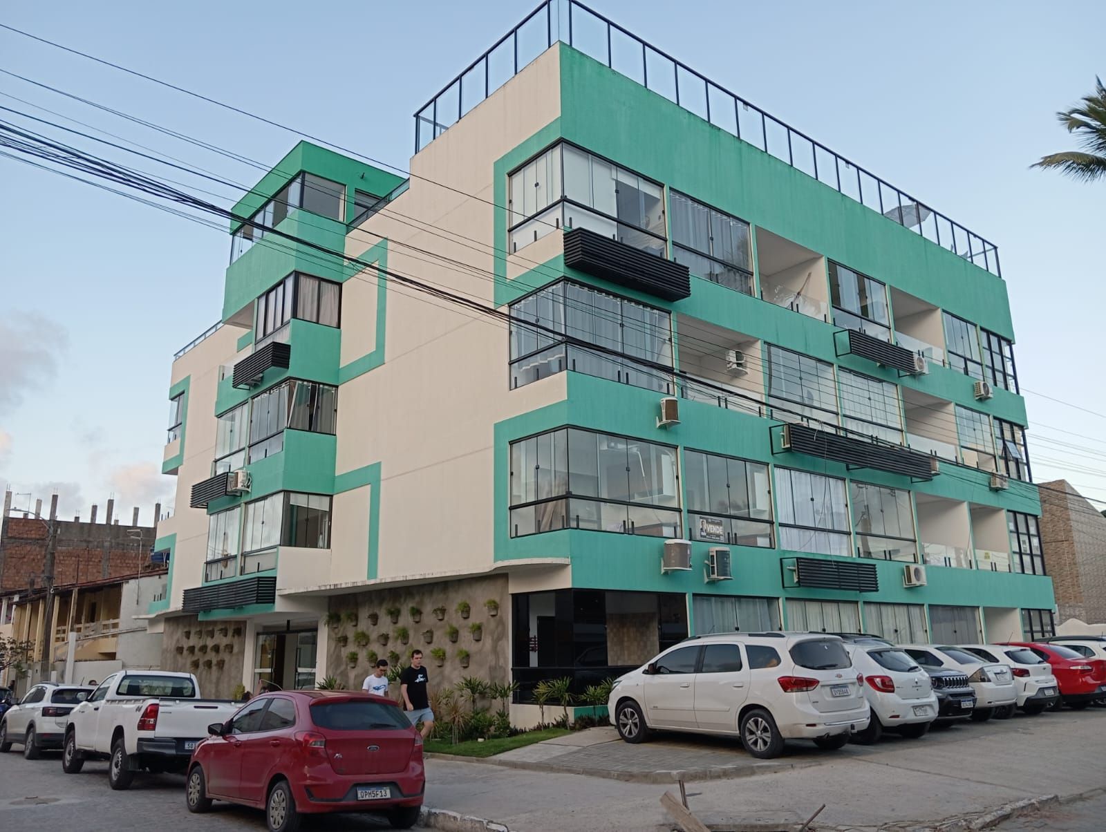 Un edificio de varios pisos con fachada verde y beige, varios balcones y coches estacionados al frente.