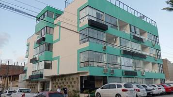 Un edificio de varios pisos con fachada verde y beige, varios balcones y coches estacionados al frente.