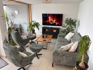 A modern living room with a flat-screen TV, green upholstered furniture, and potted plants. - LakeView Deluxe - Best Lake View (Friedrichshafen)