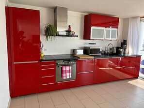 A modern kitchen with red cabinetry, a stainless steel oven, and a microwave. - LakeView Deluxe - Best Lake View (Friedrichshafen)