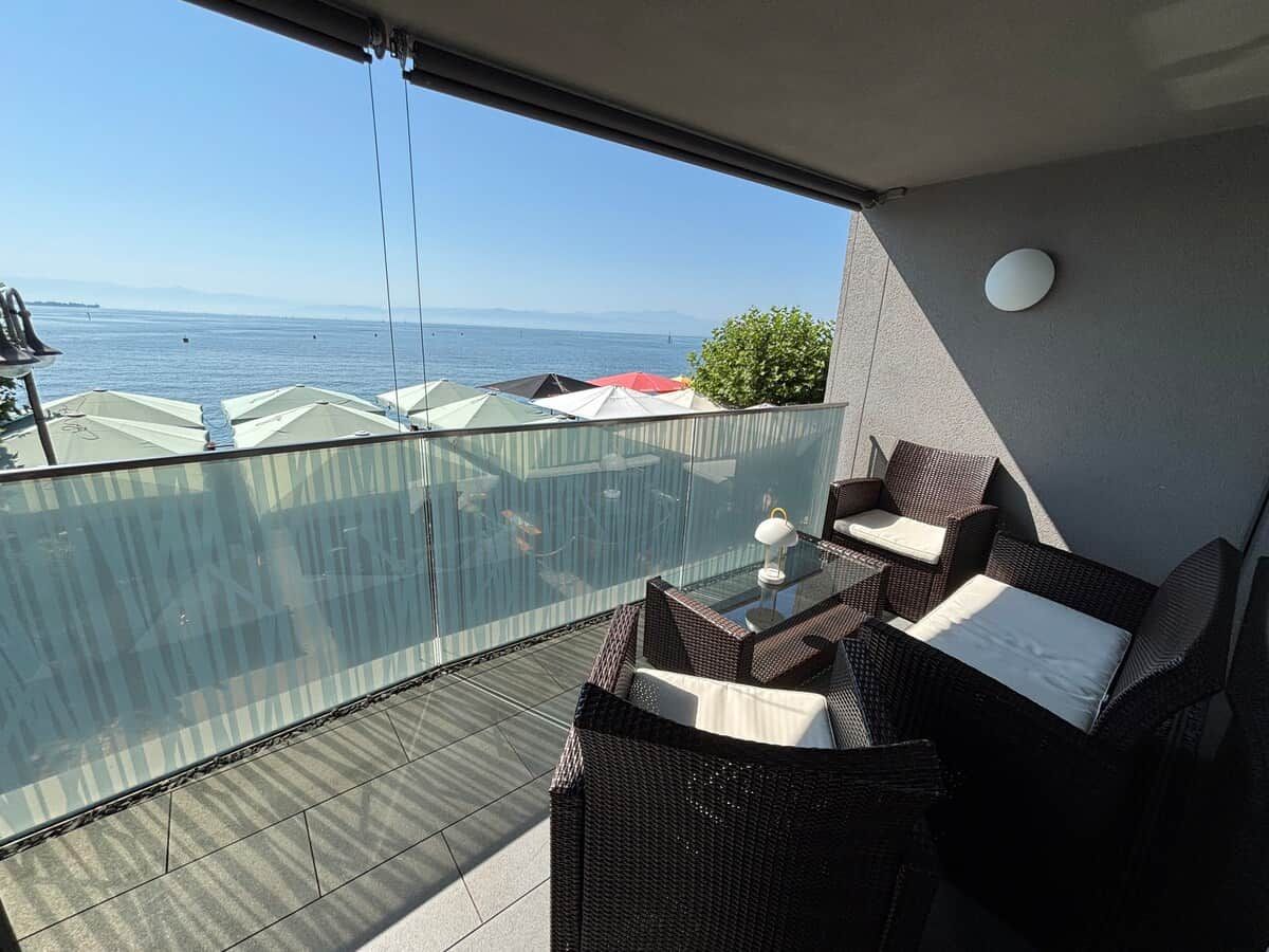 Een balkon met rieten meubilair, een glazen balustrade en uitzicht op zee.