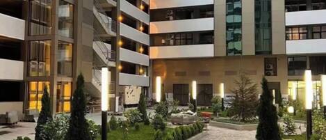 Un edificio de varios pisos con un patio central, rodeado de vegetación y un camino pavimentado.