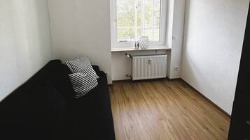 Ein Zimmer mit einer schwarzen Couch, einem Fenster mit Blick, einer Heizung und einer Deckenleuchte.