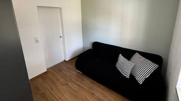 Une pièce avec un canapé noir, des coussins à motifs, un plancher en bois et une porte blanche.