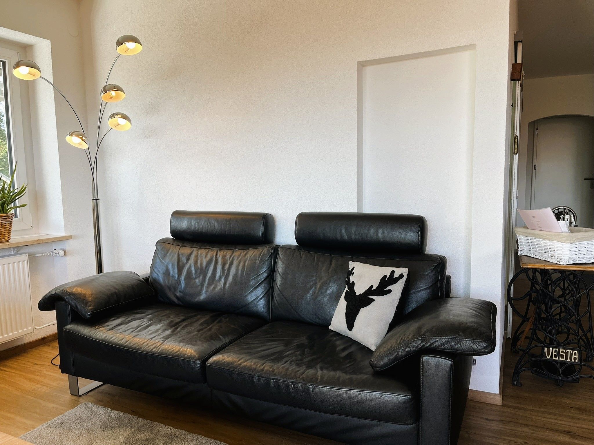 A black leather sofa with a decorative pillow against a white wall, a floor lamp, and a radiator.