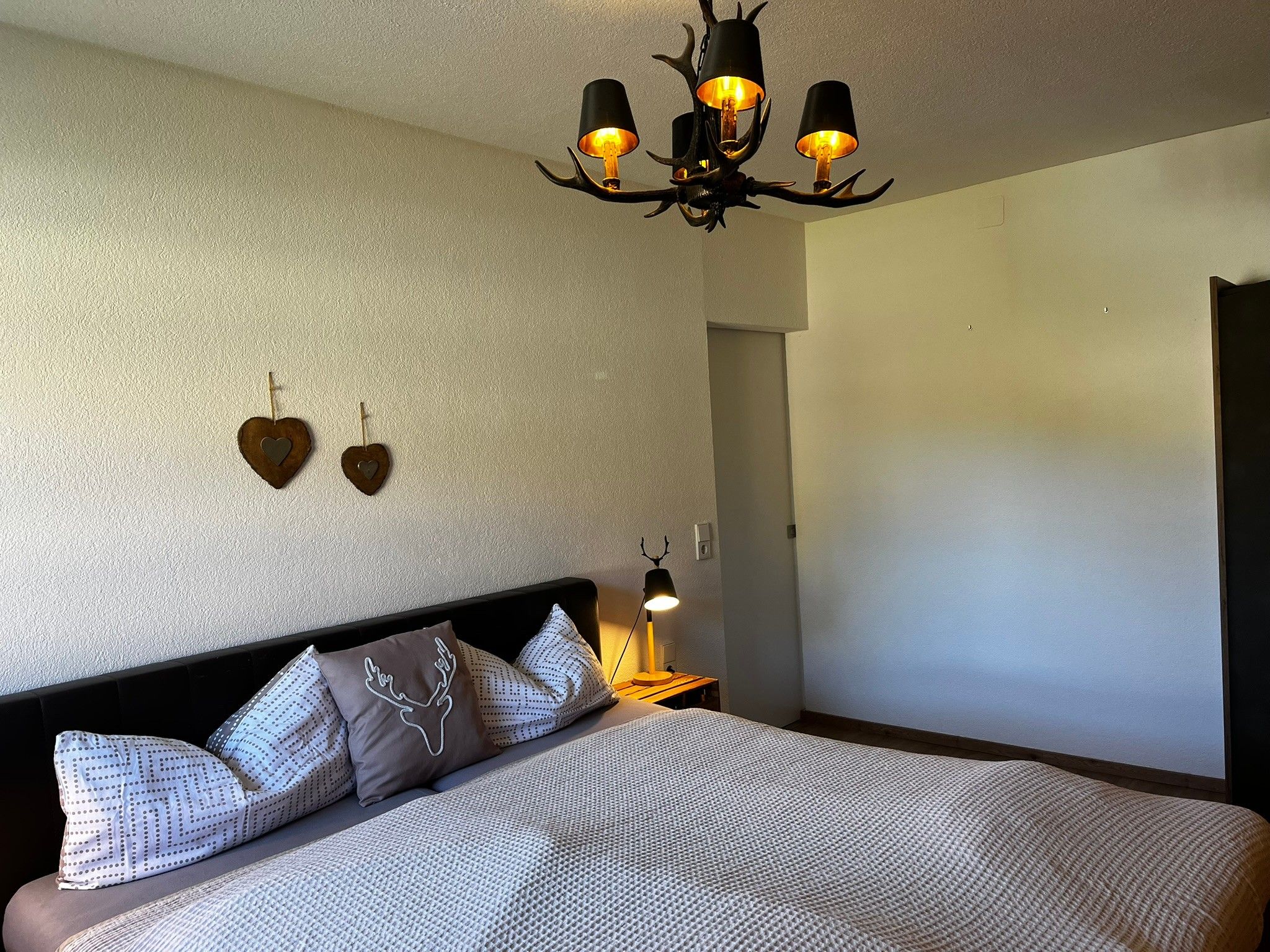A bedroom with a large bed, a wall-mounted lamp, and a ceiling light fixture.
