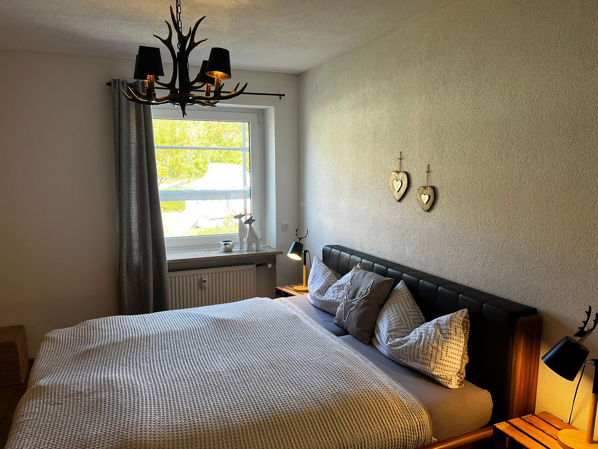 A bedroom with a bed, a window, a chandelier, and wall decorations.