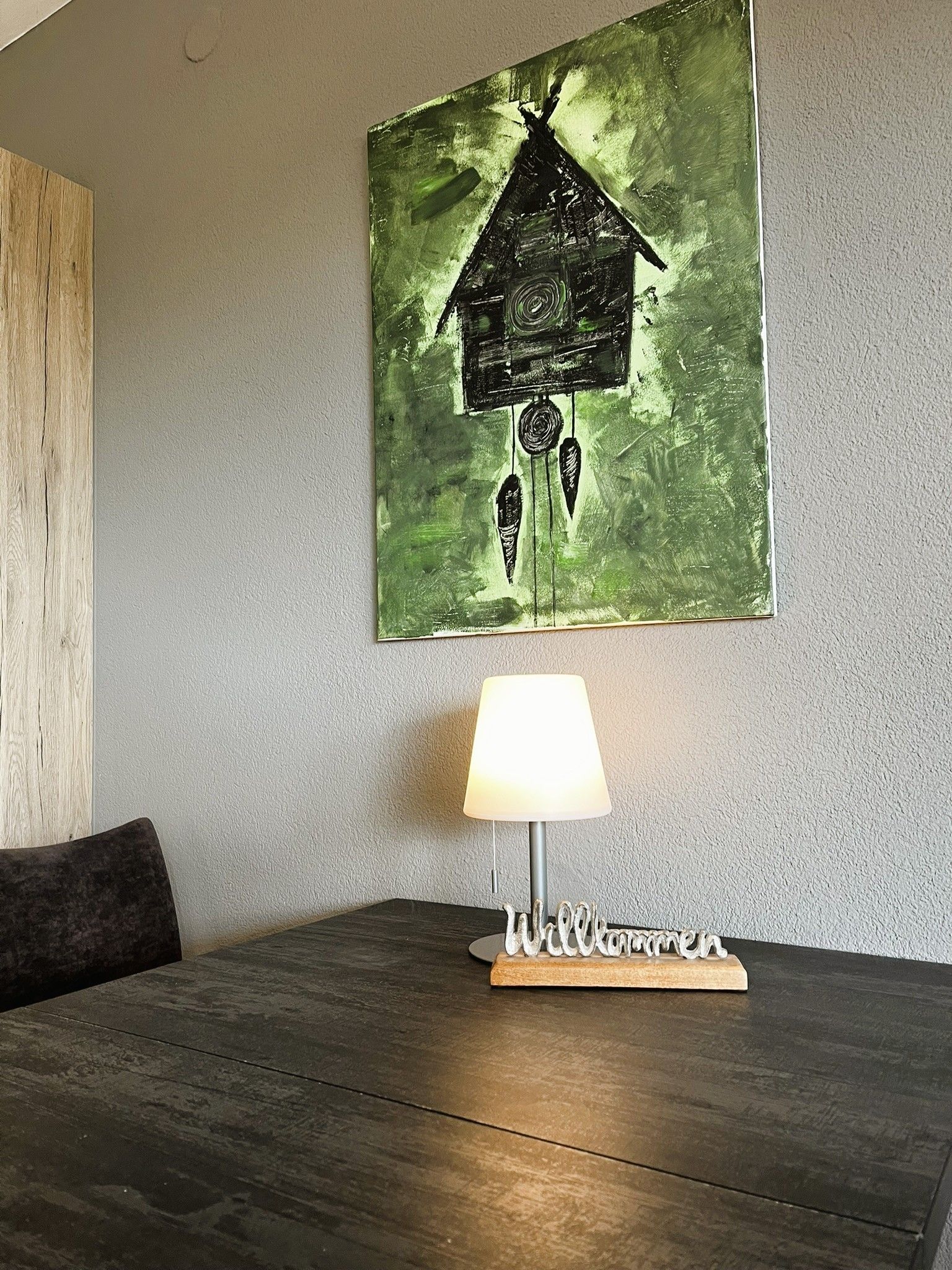 A room with a wooden table, a lamp, and a wall-mounted painting.