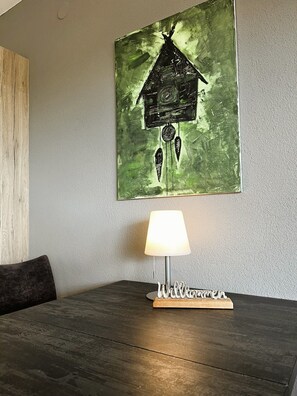 A room with a wooden table, a lamp, and a wall-mounted painting. - Apartment 'Hirschwerk' with Mountain View, Shared Garden and Wi-Fi (Lenzkirch)