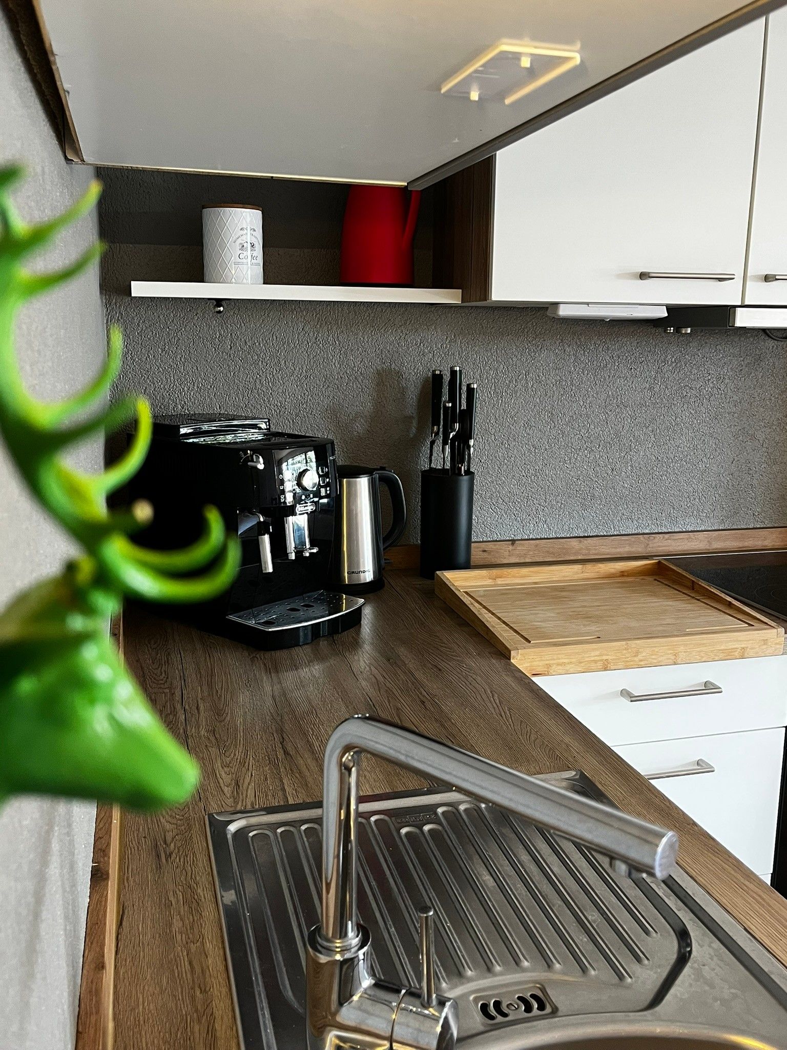A compact kitchen with a coffee machine, a kettle, and a knife block.