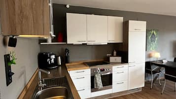 Et moderne køkken med hvide skabe, en stålvask, en kaffemaskine og et spiseområde med et bord og stole.