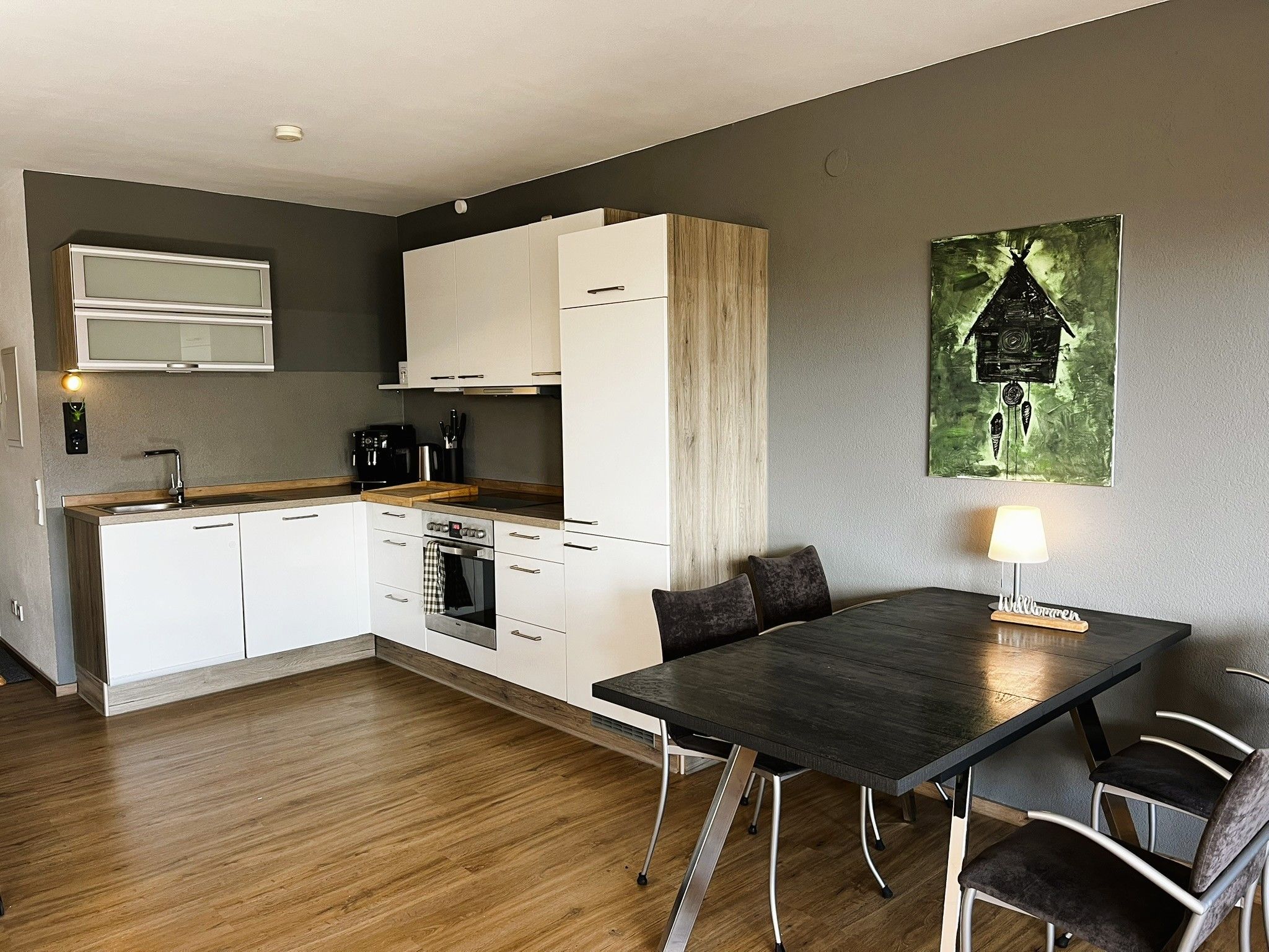 A modern kitchen with white cabinets, a dining table with chairs, and a painting on the wall.