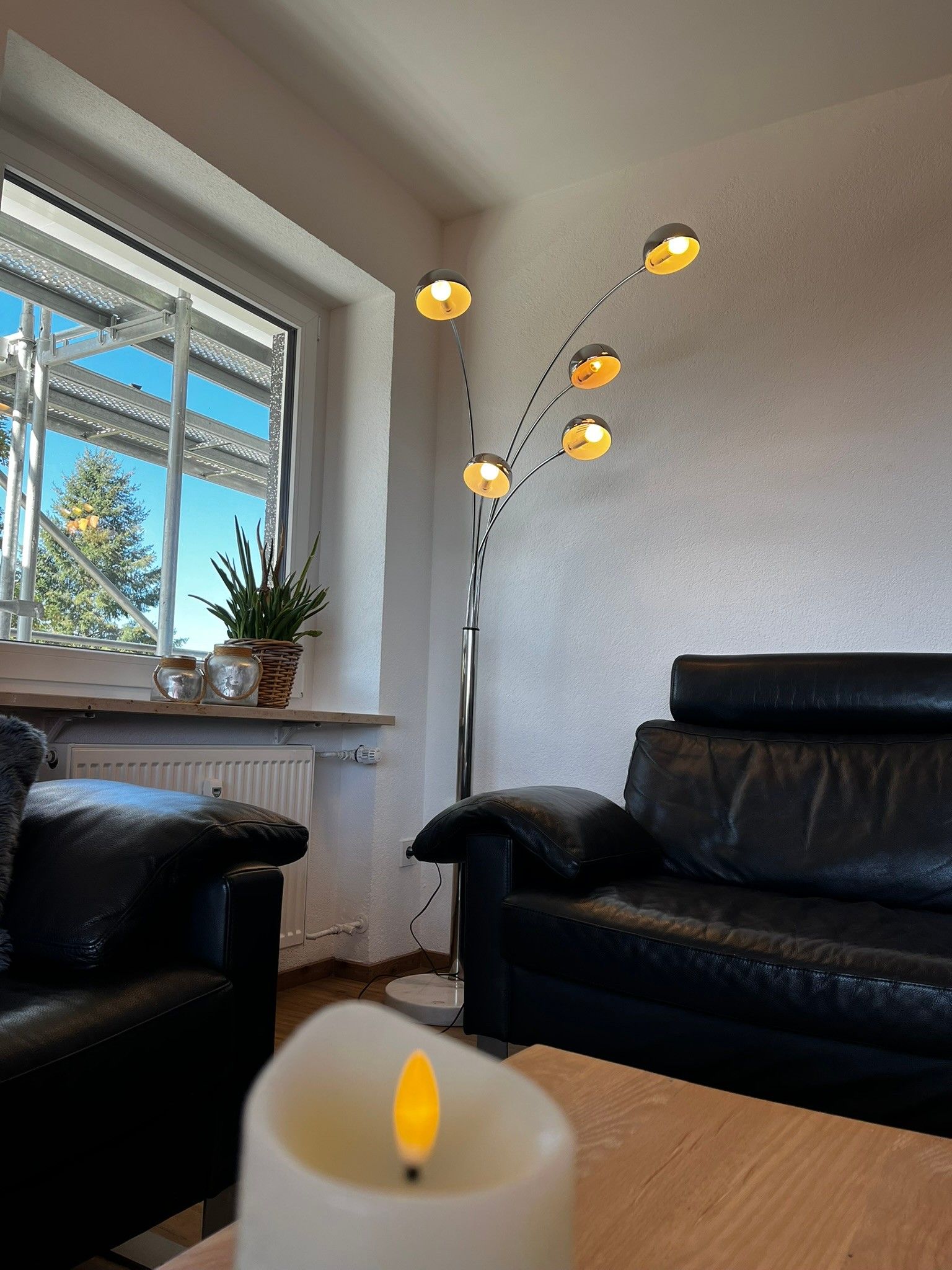 Une pièce avec un canapé en cuir noir, une table blanche sur laquelle est posée une bougie allumée et un lampadaire doté de plusieurs ampoules.