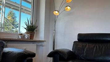 Une pièce avec un canapé en cuir noir, une table blanche sur laquelle est posée une bougie allumée et un lampadaire doté de plusieurs ampoules.