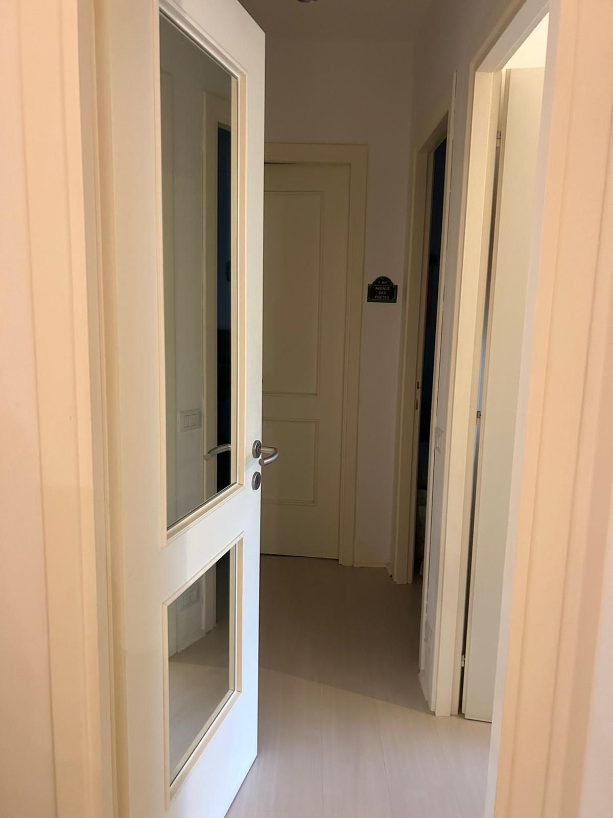 Un couloir avec une porte donnant sur une pièce, une porte avec une pancarte et une porte avec une poignée.