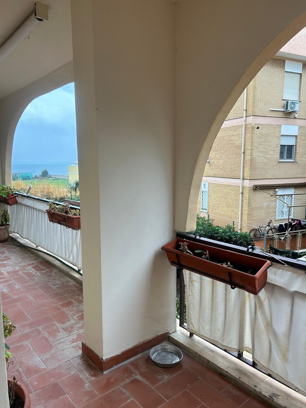 Un balcon agrémenté de plantes en pot, un récipient en métal et une vue sur la mer.