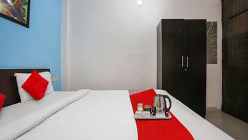A hotel room with a bed, a red throw, a tray with a coffee pot, and a wardrobe.