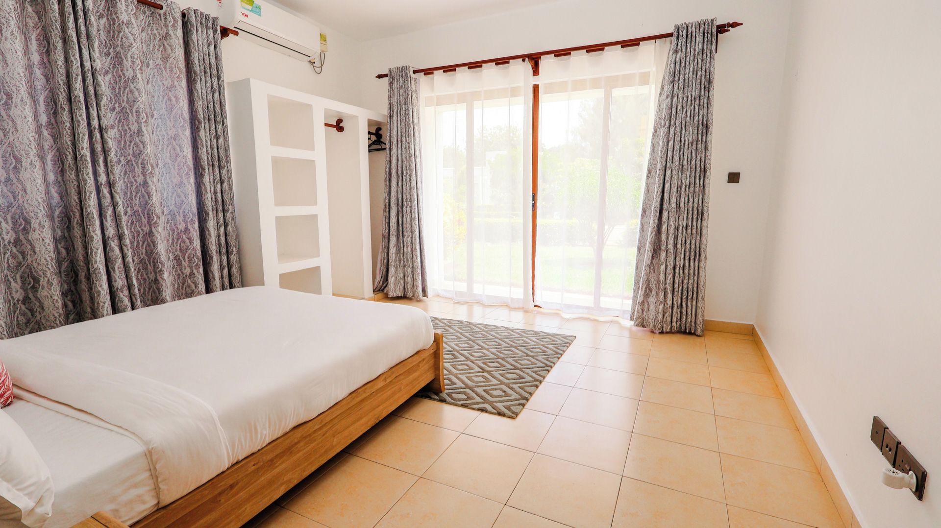 Un dormitorio con cama, armario, puerta corrediza de vidrio a un balcón y una alfombra estampada.