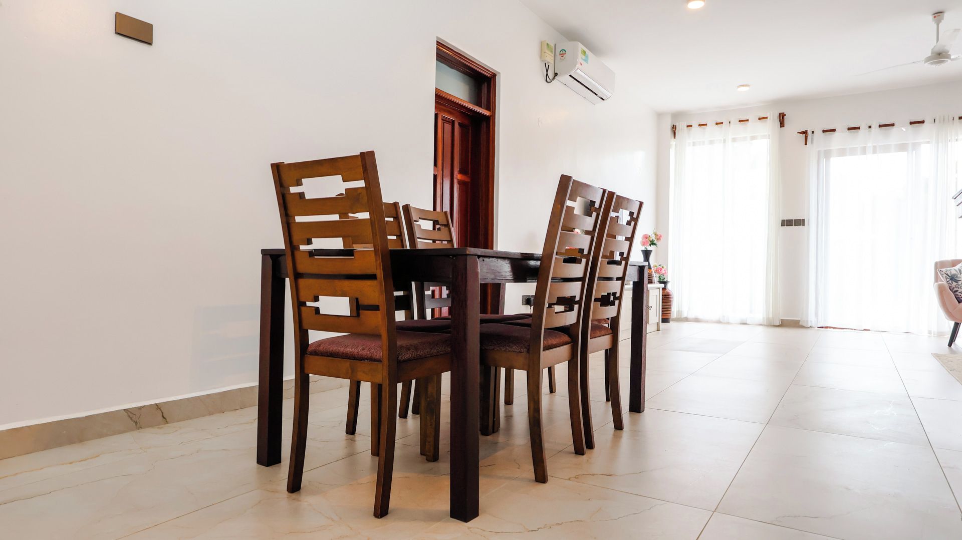 Un comedor con una mesa redonda y cuatro sillas, una puerta de madera y un ventanal con cortinas.