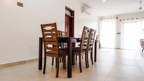 Uma sala de jantar com uma mesa redonda e quatro cadeiras, uma porta de madeira e uma janela com cortinas.
