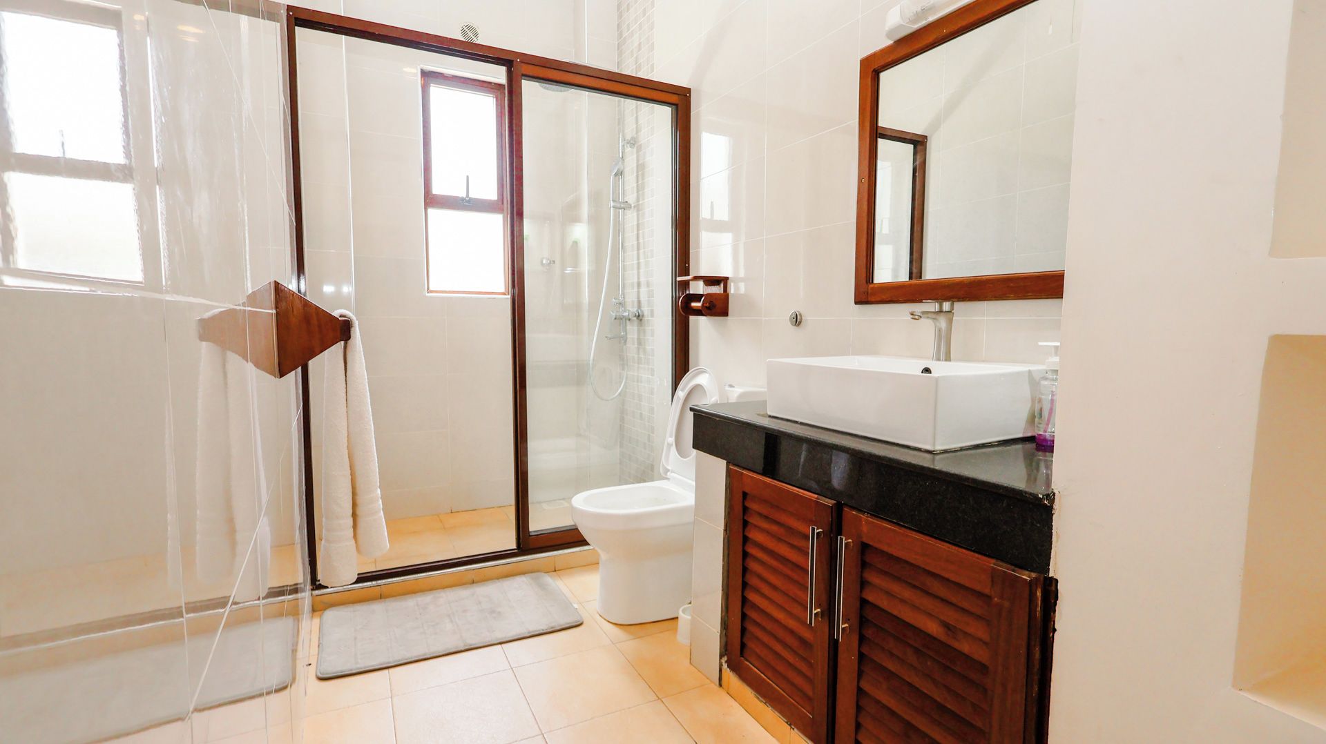 Un baño con ducha de vidrio, inodoro blanco, lavamanos con espejo y armarios de madera.