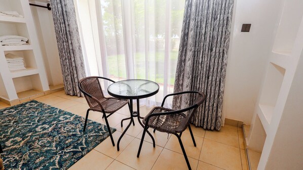 Une pièce avec une table à plateau en verre et deux chaises en osier, un tapis à motifs bleus et une étagère blanche où sont pliées des serviettes.