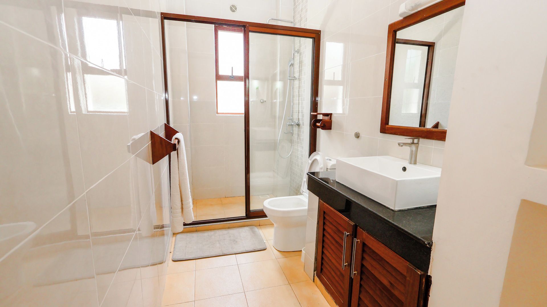 A bathroom with a glass shower door, a white toilet, a sink with a mirror, and wooden cabinets.
