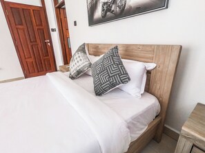 Un lit avec une tête de lit en bois, deux coussins à motifs et un couvre-lit blanc.