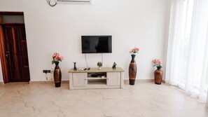 Un salon avec un téléviseur à écran plat fixé au mur, un meuble en bois servant de support pour le téléviseur, et deux vases ornés de fleurs.