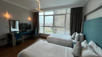 Una habitación de hotel con cama, escritorio, televisor y un amplio ventanal con vista a la ciudad.