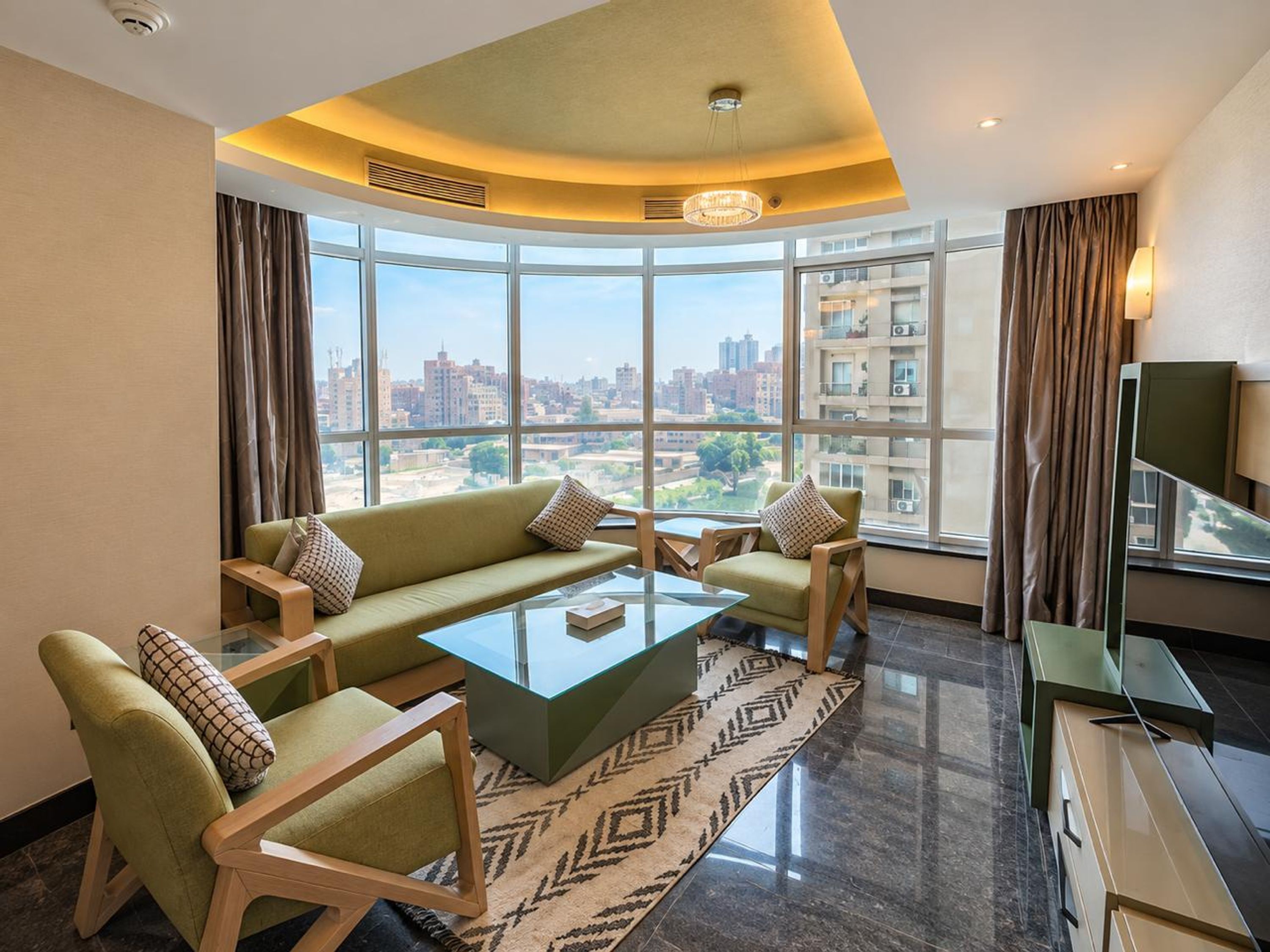 Una sala moderna con un sofá, sillones, una mesa de centro y vistas de un paisaje urbano a través de amplios ventanales.