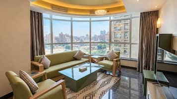 Una sala moderna con un sofá, sillones, una mesa de centro y vistas de un paisaje urbano a través de amplios ventanales.