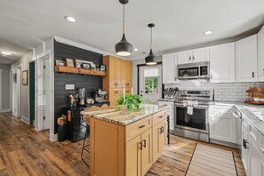 A modern kitchen with white cabinets, a central island, and a microwave. - The Social Canvas | Spacious & Cozy | Fire Pit, Blackstone, Game Room, Espresso Machine | Pet's OK! (Charlotte)
