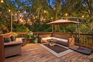 A deck with outdoor furniture, a table, and string lights. - The Social Canvas | Spacious & Cozy | Fire Pit, Blackstone, Game Room, Espresso Machine | Pet's OK! (Charlotte)