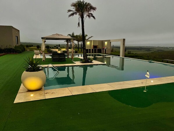 A swimming pool with a palm tree, a gazebo, and a view of the landscape.