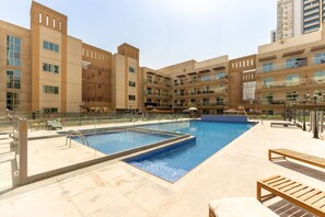A swimming pool with a tiled deck, surrounded by a multi-story building with balconies. - New York industrial style JVC (Dubai)