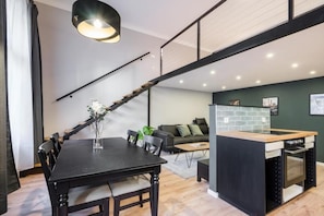 A modern kitchen with a built-in oven, a dining area with a black table and chairs, and a staircase leading to an upper level. - R38 - Boutique Apartments by BQA (Budapest)