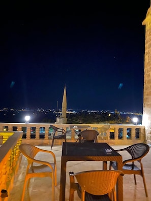 Un espacio al aire libre con mesas y sillas, con vista a un paisaje urbano de noche.