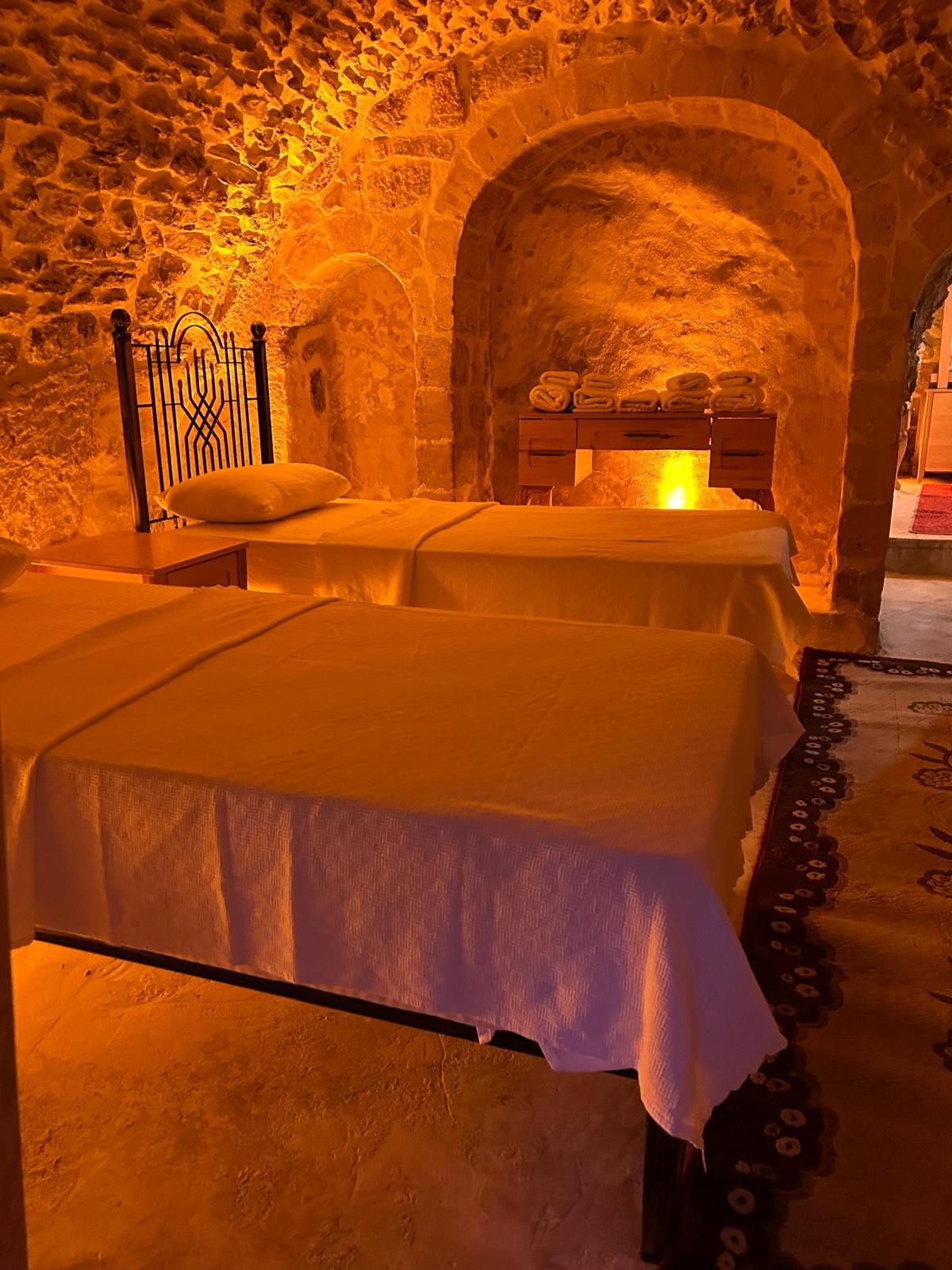 Una habitación con dos camas, una pared de piedra y un aparador de madera.