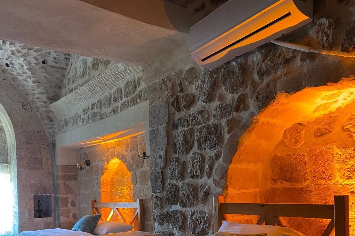 A room with two beds, stone walls, and an air conditioning unit.