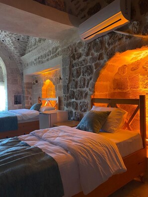 A room with two beds, stone walls, and an air conditioning unit. - ASEL KONAK (Mardin)