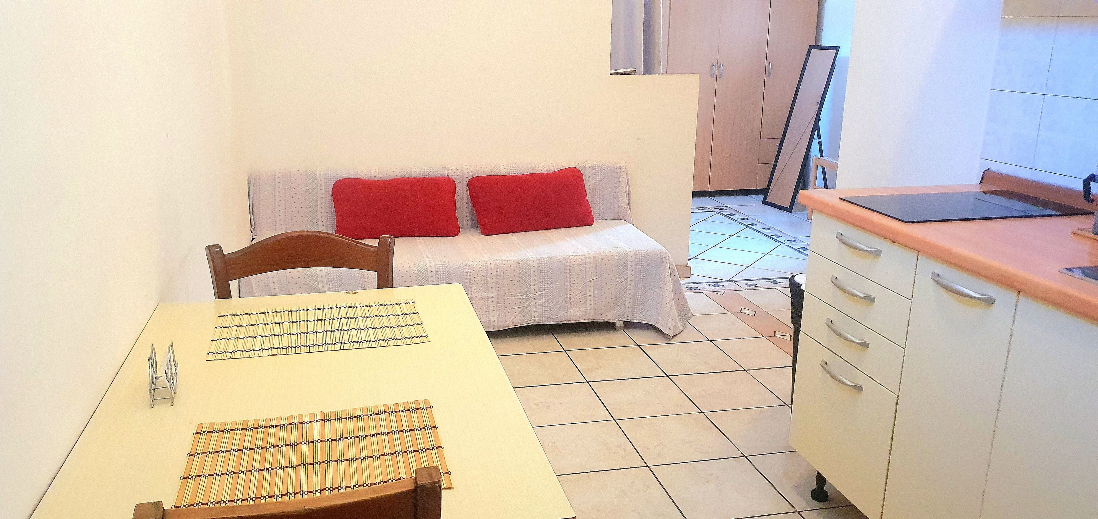 A small kitchenette with a table, chair, and a sofa with red cushions.