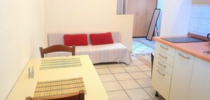 Uma pequena cozinha compacta com uma mesa, cadeira e um sofá com almofadas vermelhas.