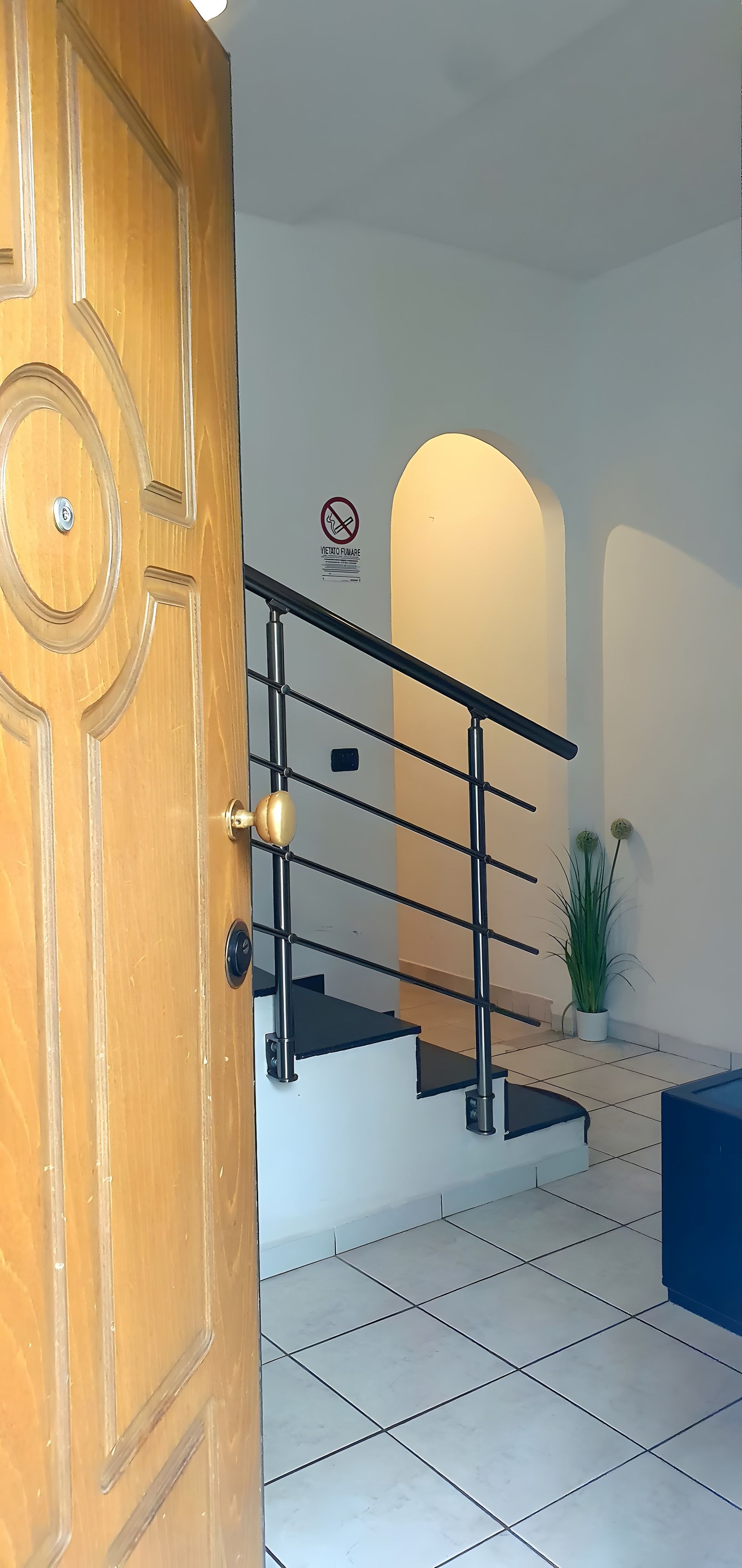 A wooden door with a brass handle, a staircase with a black railing, and a potted plant on the floor.