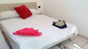 Een bed met een bedsprei met dessin, een rood kussen en een opgevouwen handdoek.
