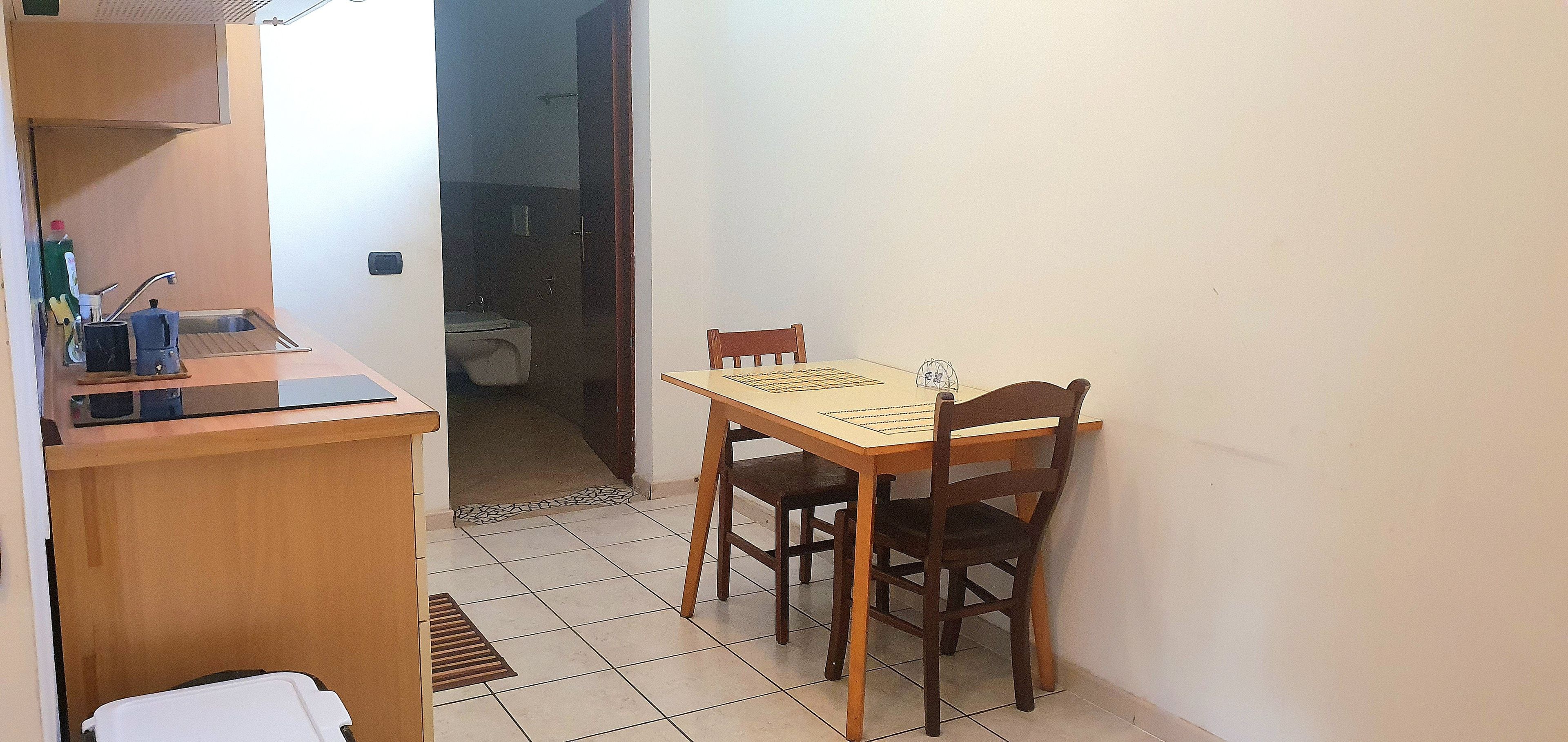 A small dining area with a wooden table and chairs, a kitchen counter with a sink, and a tiled floor.