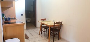 Uma pequena área de refeições com mesa e cadeiras de madeira, bancada de cozinha com pia e chão revestido de azulejos.