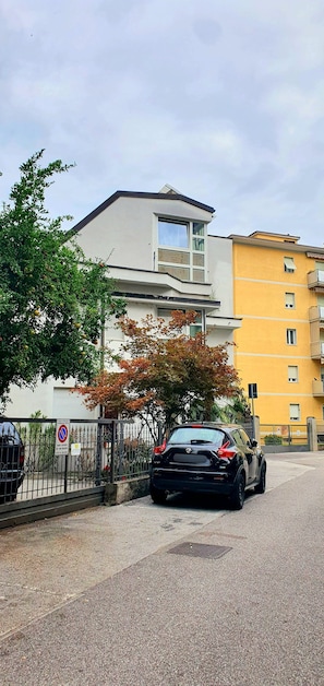 A parking area with a black car, a building with a white facade, and a yellow building in the background. - Apartment 'Appartamento con due stanze Bolzano' (Bolzano)